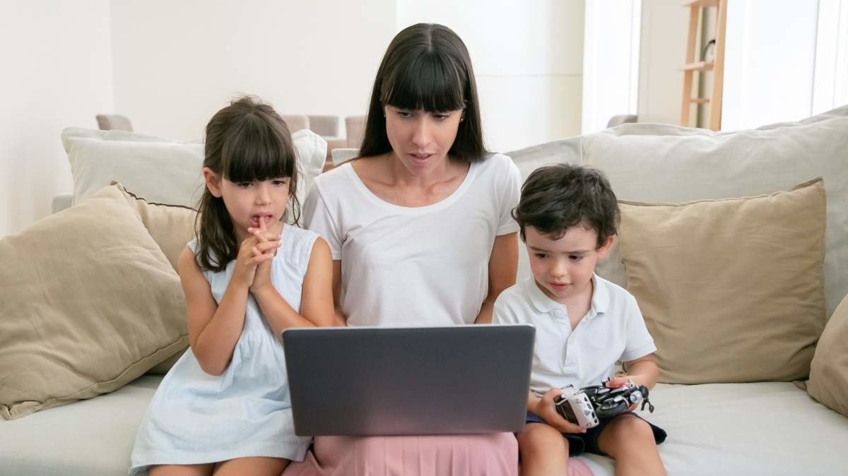 Serious mom and two worried kids watching movie on laptop in living room. Medium shot, front view. Communication or entertainment concept