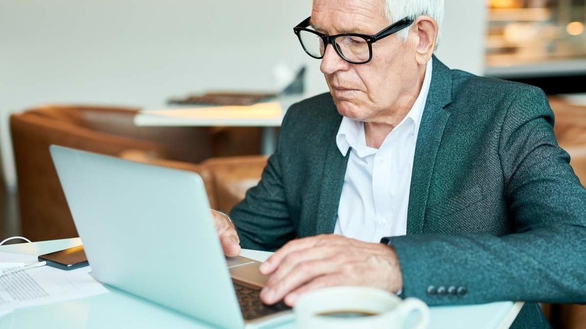 Portrait of contemporary senior businessman using laptop in cafe while working during coffee break, copy space