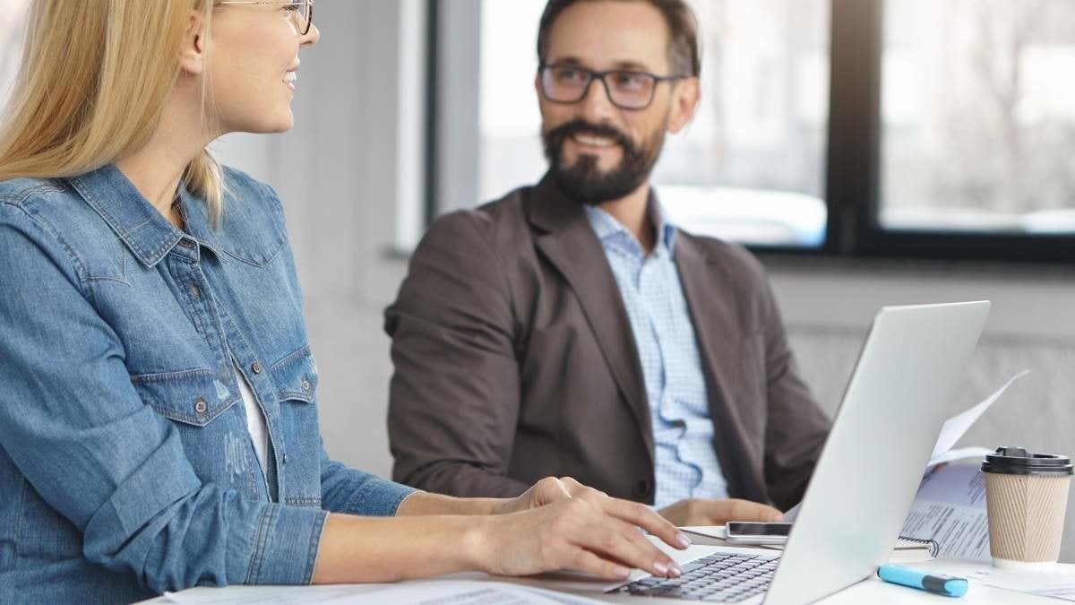 Portrait of cheerful female manager and her boss work together in office, study important documents, look at each other with happy expressions, feel sympathy, glad collaborate for common project