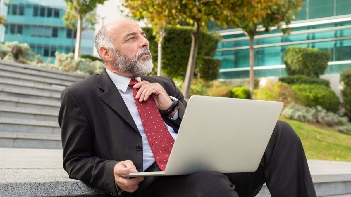 Pensive businessman using laptop on steps. Thoughtful mature businessman sitting on stairs and working with laptop computer on street. Business and technology concept