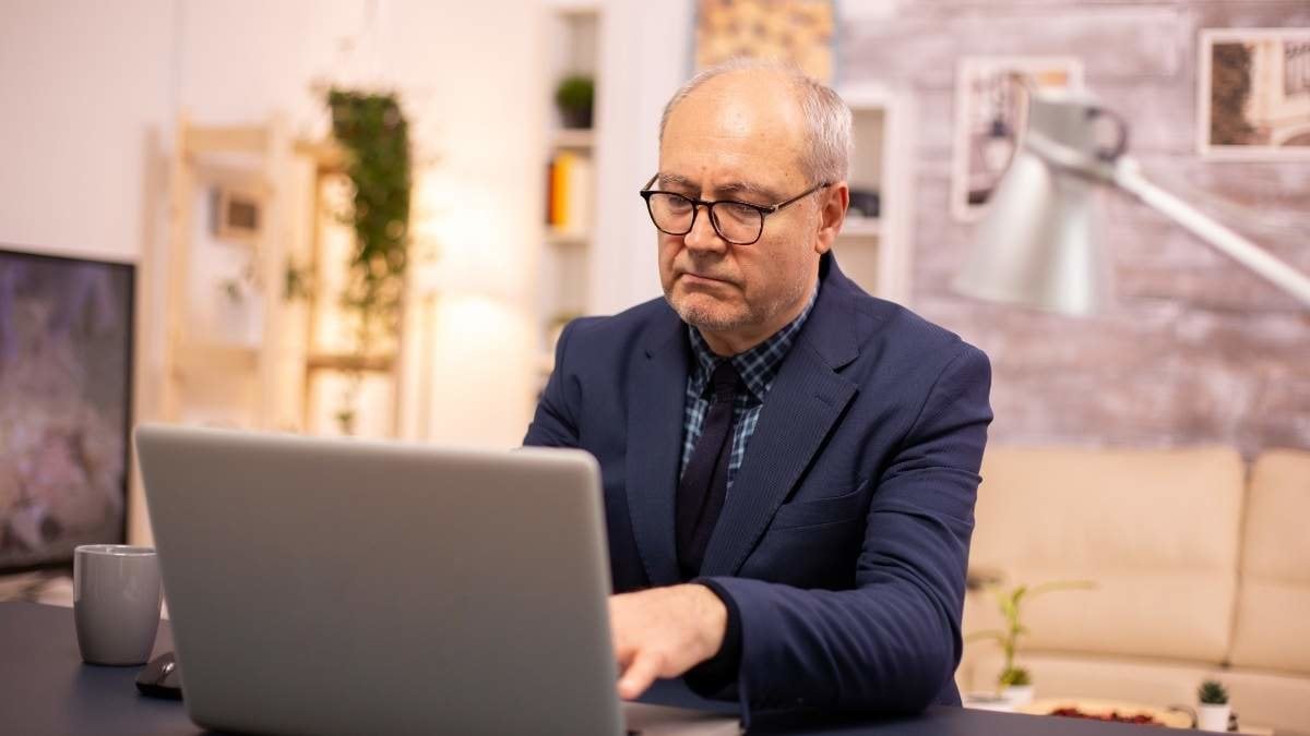 Elderly man typing on laptop in cozy living room.