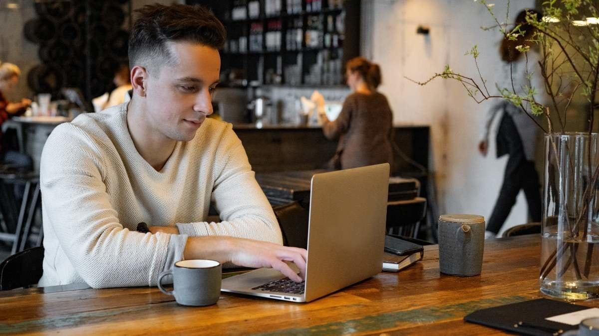 young man drinks tea and works on a laptop, freelancer working in a cafe