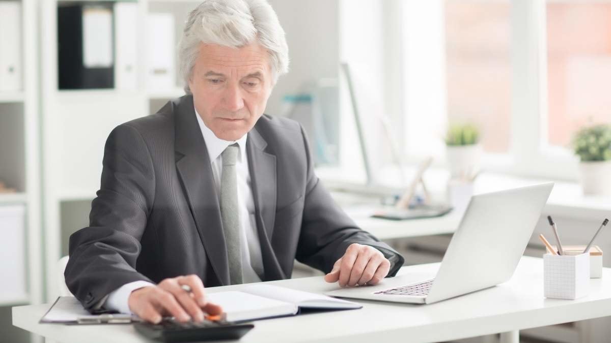 Experienced economist in suit sitting by desk in office and making calculations