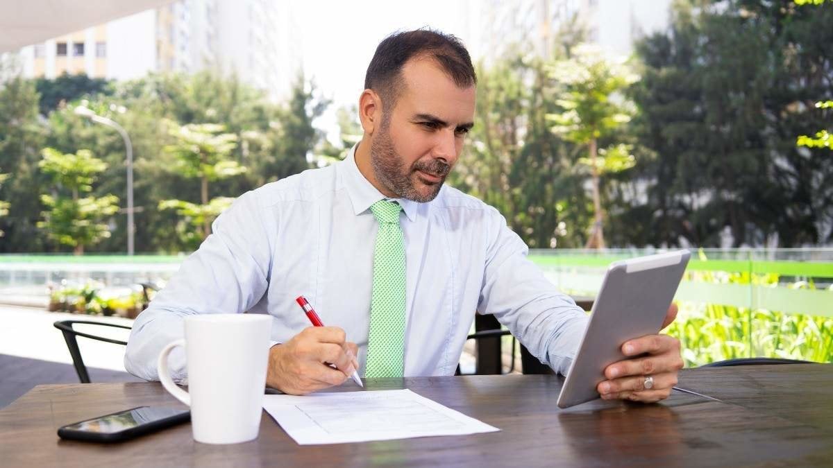 Serious mature freelancer working with digital tablet at cafe. Portrait of Caucasian businessman sitting at table and communicating to partner via pc tablet. Freelance concept