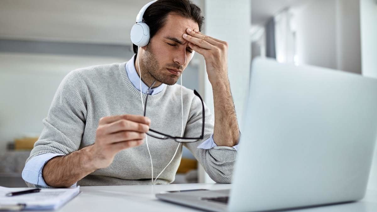 Young businessman having a headache and feeling exhausted while working on laptop at home.