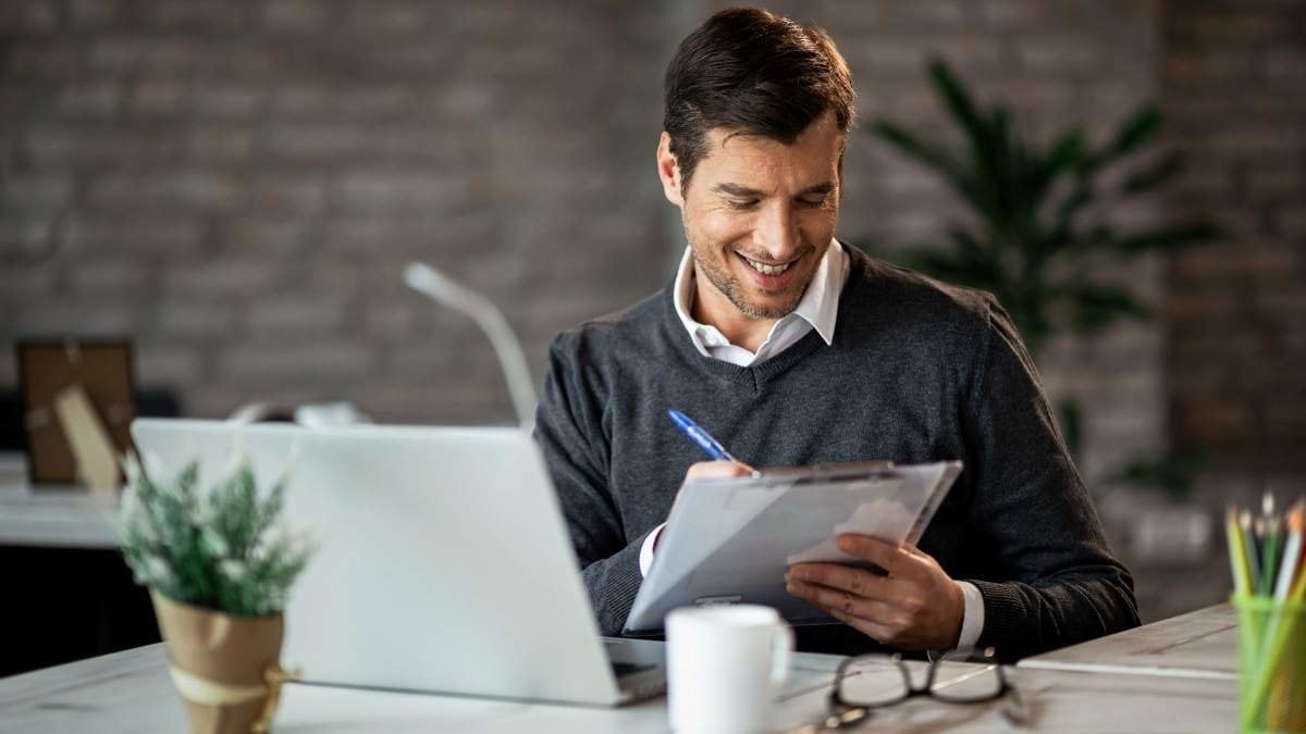 Smiling entrepreneur writing business report while working on laptop in the office.