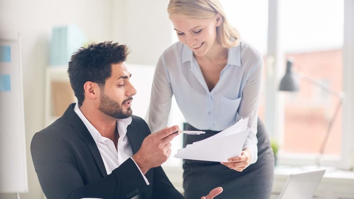 Confident employer pointing at paper in hands of his subordinate and asking her to have them signed