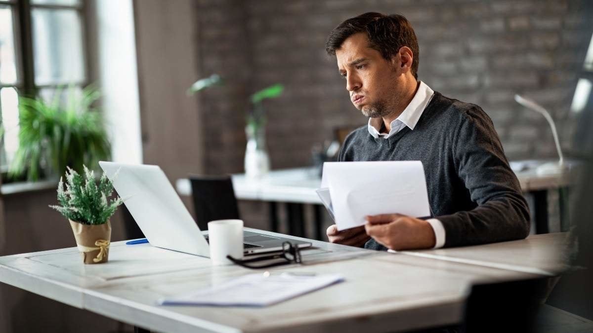 Overworked businessman using laptop while going through business reports and working in the office.