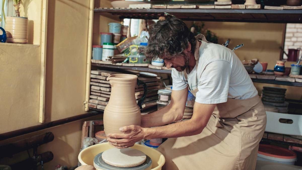 Creating a jar or vase of white clay close-up. Master crock. Man hands making clay jug macro. The sculptor in the workshop makes a jug out of earthenware closeup. Twisted potter's wheel.