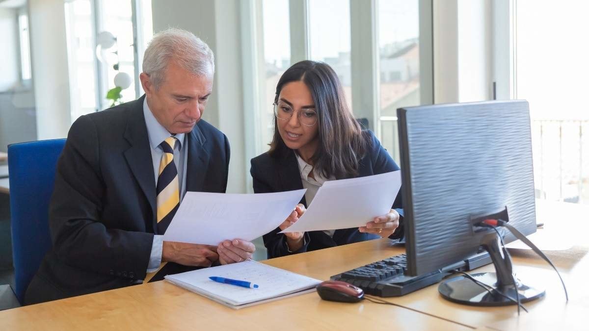 Female professional explaining document details to client at workplace. Serious business leader consulting financial or legal expert. Teamwork or cooperation concept