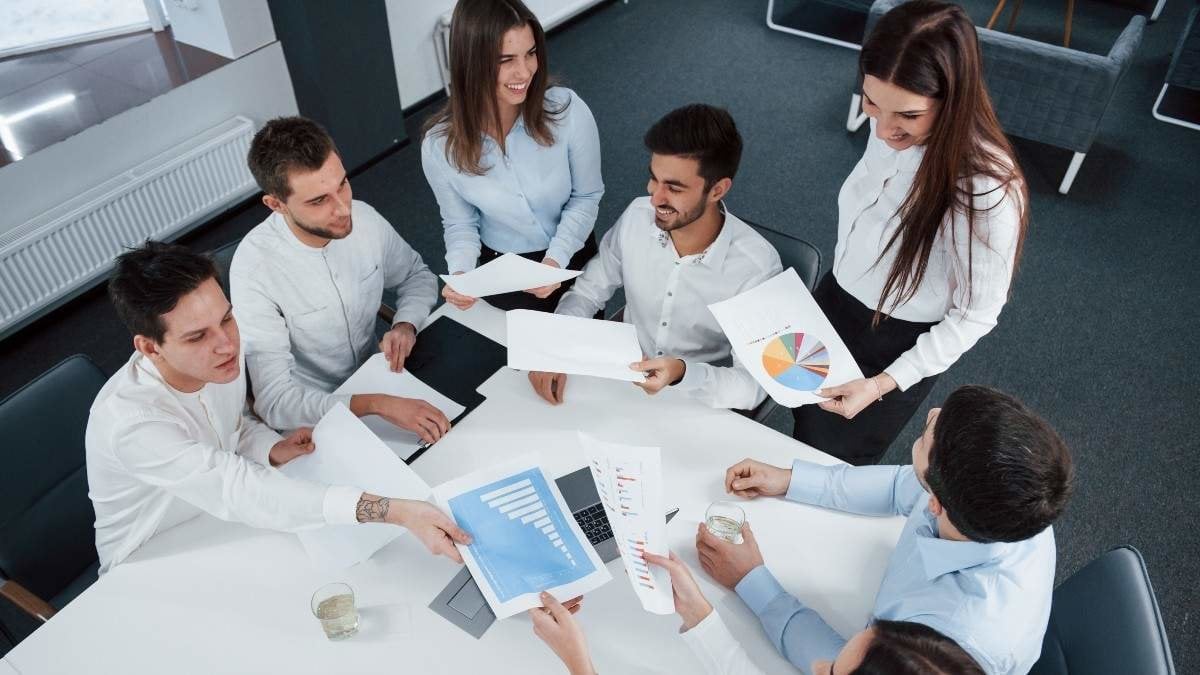 So young but so successful. Top view of office workers in classic wear sitting near the table using laptop and documents.